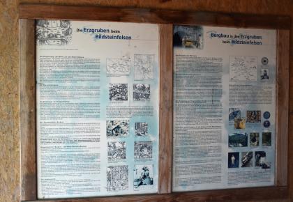 Informationstafel zum früheren Bergbau beim Bildsteinfelsen Blick auf eine zweiteilige Schautafel aus Holz. Die Tafel zeigt Texte, Zeichnungen und Fotos zum Thema Erzgruben beim Bildsteinfelsen sowie den früheren Bergbau in diesen Gruben.
