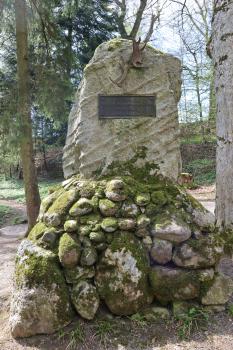 Blick auf ein Denkmal, errichtet aus Anlass steinzeitlicher Funde. Das Denkmal besteht aus mehreren Findlingen, bemoost und unterschiedlich groß, sowie einem aufgesetzten grauen Steinblock. Am Block befindet sich neben einer Tafel ein Geweihstück.