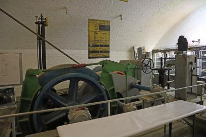 Fördermaschine im Silberbergwerk Teufelsgrund bei Münstertal Blick in einen Ausstellungsraum des Besucherbergwerks Teufelsgrund mit heller, gewölbter Decke. Im Vordergrund steht eine große Fördermaschine mit blaugrauem Schwungrad.