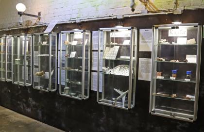 Ausstellung zu Rohstoffen und daraus hergestellten Produkten im Silberbergwerk Teufelsgrund bei Münstertal Blick auf mehrere verglaste Ausstellungskästen mit Rohstoffen wie Kupfer und Aluminium. Gezeigt werden auch daraus hergestellte Produkte wie etwa Bleche, Besteck und Münzgeld.