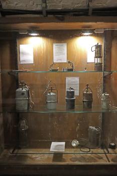 Vitrine mit historischen Grubenleuchten im Silberbergwerk Teufelsgrund bei Münstertal Blick auf eine hölzerne Vitrine mit Glasböden im Besucherbergwerk Teufelsgrund. Ausgestellt sind historische Grubenleuchten, wie etwa Karbidlampen sowie eine Froschlampe.