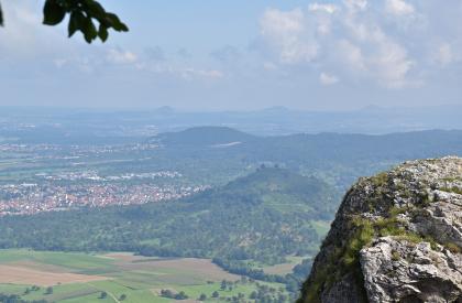 Blick vom Breitenstein nach Nordosten auf das Albvorland mit den Vulkanit-Erhebungen Limburg und Turmberg Blick aus großer Höhe auf Felder und bewaldete Berge. Links sind mehrere Ortschaften verteilt. Rechts vorne ist ein vorspringender Felsenkopf ganz nahe. Im dunstigen Hintergrund verläuft ein Höhenzug mit drei markanten Erhebungen.