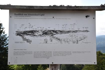 Informationstafel zu Geologie und Landschaft – Blick vom Schauinslandgipfel nach Süden und Osten Das Bild zeigt eine Schautafel vom Schauinsland-Gipfel. Darauf ist eine mit Namen versehene Zeichnung von Bergen sowie Ortschaften, die man von diesem Standort aus sehen kann. Dazu wird der Abschnitt Hinterwaldkopf – Belchen näher erläutert.