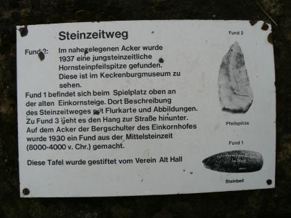 Informationstafel zu steinzeitlichen Fundstücken auf dem Einkorn Hier wird eine schon leicht beschädigte Informationstafel gezeigt, mit Bildern und Text zu steinzeitlichen Fundstücken wie Pfeilspitze und Steinbeil.