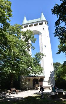 Die „Pfullinger Unterhose“ – Aussichtsturm auf dem Schönberg südlich von Pfullingen Blick auf einen Aussichtsturm, der aus zwei hohen weißen Säulen sowie oben aus einem bogenförmigen Brückenbau besteht. Der Doppelturm steht frei, der Blick auf ihn wird jedoch von davor befindlichen Bäumen fast verdeckt.