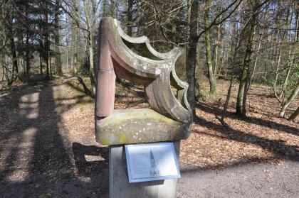 Neben dem Eichbergturm steht dieses Maßwerk aus Heimbacher Buntsandstein, das früher im Turm des Freiburger Münsters eingebaut war. Blick auf ein aus rotem Sandstein gefertigtes Bauteil des Freiburger Münsters, im Freien aufgestellt. Im Hintergrund stehen zahlreiche Bäume.