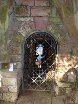 Blick auf den mit einer Gittertür verschlossenen Eingang eines Bergwerks. Die Tür ist in mehrfarbiges Mauerwerk eingelassen.