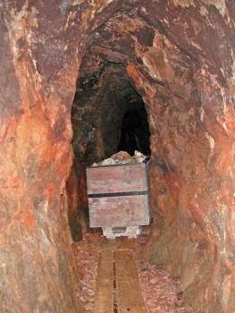 Beladener Hund in einem der Stollen der Grube Segen Gottes bei Haslach im Kinzigtal Blick in einen alten Bergwerksstollen mit im Vordergrund orangefarbenen, eng stehenden Wänden. Im Mittelgrund steht ein altes Transportfahrzeug aus Holz, es ist mit Gestein beladen.