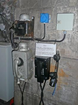Das Bild zeigt mehrere alte Telefonanlagen, mit schwarzen und silbernen Gehäusen sowie Hörern, wie sie früher in Bergwerken verwendet wurden. Heute dienen sie als Vorzeigemuster in einem Besucherbergwerk.