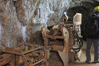 Wurfschaufellader und hinterer Teil eines Bohrwagens im Besucherbergwerk Finstergrund bei Wieden Gezeigt werden hier ehemalige Arbeitsgeräte in einem Besucherbergwerk: Wurfschaufellader und Bohrwagen, abgestellt vor einer linksseitig verlaufenden grauen Stollenwand.