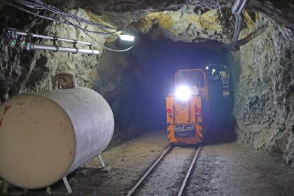 Grubenbahn im Besucherbergwerk Finstergrund bei Wieden Das Bild zeigt eine beleuchtete Grubenbahn auf Schienen im Besucherbergwerk Finstergrund. Die Bahn - rechts im Bild - fährt durch einen schmalen, niedrigen Tunnel. Links an der Stollenwand ist ein Benzin- oder Öltank aufgestellt.