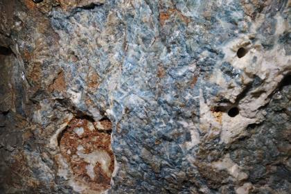 Reste von Flussspat an der Stollenwand im Besucherbergwerk Finstergrund bei Wieden Nahaufnahme einer Gesteinswand im Besucherbergwerk Finstergrund. In der Bildmitte zeigen sich Reste von blauem Flussspat, links unten platzt braunes Gestein hervor. Rechts sind weißliche Stellen mit Bohrlöchern zu erkennen.