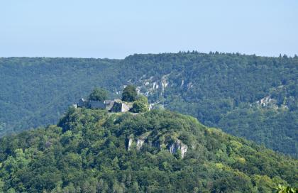 Vom Eppenzillfelsen aus gesehen erblickt man hinter der Ruine Hohenurach auf der Nordseite des Ermstals eine Felsreihe im Oberjura Blick auf einen bewaldeten Bergkegel mit einer Burgruine auf der Kuppe und vorstehenden Felsen etwas darunter. Im Hintergrund verlaufen bewaldete Berge mit ebenen Kuppen. An deren Hängen sind ebenfalls Felsformationen zu erkennen.