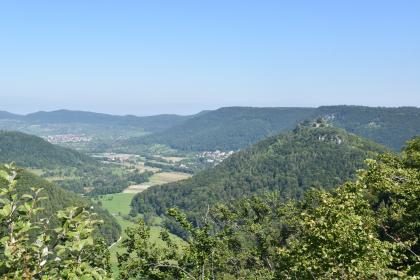 Blick vom Eppenzillfelsen nach Nordwesten durchs Brühlbachtal ins Ermstal Blick von erhöhtem Standort auf einen rechts aufsteigenden bewaldeten Bergkegel mit einer Burg. Links schlängelt sich ein teils besiedeltes Tal zwischen weiteren Bergen hindurch.