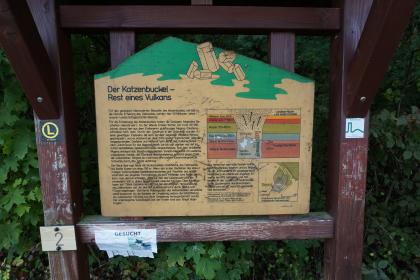 Schautafel am geologischen Lehrpfad „Weg der Kristalle“ auf dem Katzenbuckel im Odenwald Blick auf eine hölzerne, oben wie ein Berg geformte Schautafel eines geologischen Lehrpfades. Thema der Tafel: „Der Katzenbuckel - Rest eines Vulkans“.