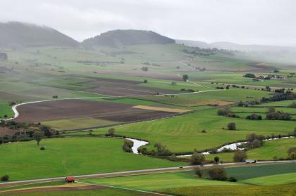Blick vom Wartenberg über die Donauaue nach Südwesten zum Fürstenberg Von erhöhtem Standpunkt aus blickt man auf eine hügelige Landschaft mit Wiesen und Äckern. Links verlieren sich Berghänge im Dunst. Die Kuppen der Berge sind bewaldet. Im Vordergrund rechts schlängelt sich ein schmaler Fluss.