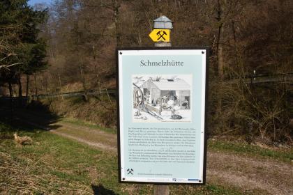 Infotafel am bergbauhistorischen Lehrpfad Birkenberg bei Bollschweil-St. Ulrich Blick auf eine farbige Schautafel am bergbauhistorischen Lehrpfad Birkenberg. Die Tafel steht vor einem Waldhang sowie einem Fahr- und Wanderweg und erzählt von Schmelzhütten. Gezeigt wird auch eine Darstellung eines früheren Hüttenwerks.