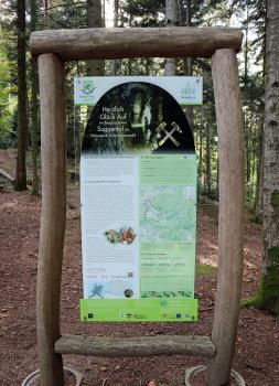 Informationstafel an der Station „Urgraben“ des Bergbauwanderpfads Silbersteig in Waldkirch-Suggental Blick auf eine von Holzstämmen eingefasste Schautafel des Silbersteigs Suggental. Die Tafel berichtet über die Wasserversorgung des Bergwerks mittels Grabenbau, einem für das Mittelalter technischen Wunderwerk.