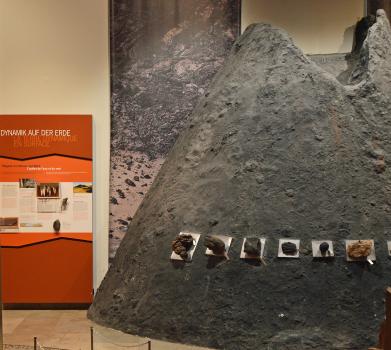 Modell eines Vulkans im Ausstellungsteil „Geologie am Oberrhein“ des Staatlichen Museums für Naturkunde Karlsruhe Blick in einen Ausstellungsraum des Staatlichen Museums für Naturkunde Karlsruhe. Thema des Raumes ist die „Geologie des Oberrheins“. Rechts steht die Nachbildung eines schwärzlichen Vulkankegels mit Gesteinsfunden. Links steht eine farbige Infotafel.
