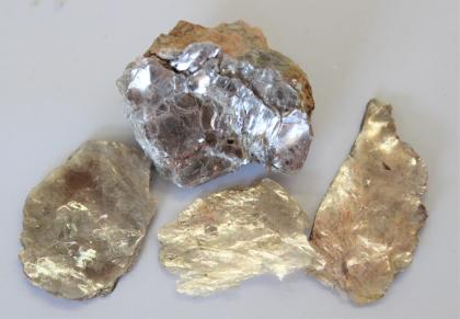 Großaufnahme von vier Gesteinsstücken. Die untere Reihe zeigt drei Handstücke in Gold- und Bronzetönen, darüber liegt ein etwas größeres, teils silberfarbenes Stück.