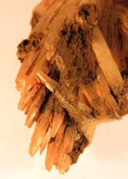 Calcit-Kristalle aus der Grube Gottes Ehre Großaufnahme vom unteren Ende eines orangeroten Gesteinsstückes. Das Gestein besteht aus dünnen, bleistiftähnlichen Kristallen, die überwiegend abwärts ausgerichtet sind. Rechts finden sich auch quer verlaufende Kristalle, die teils abgebrochen sind.