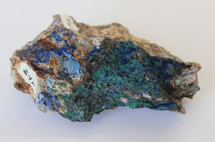 Großaufnahme eines kleinen, sternförmig gekerbten Gesteinsstückes. Auf einer bräunlichen Oberfläche zeigen sich links kleine blaue, rechts größere grüne Einlagerungen.