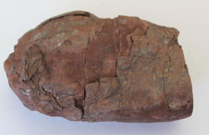 Hämatit-Geode aus dem Steinbruch am Rebio In Großaufnahme fotografiertes Handstück von rotbraunem Hämatit. Oben und links sind die Kanten gerundet. In der Bildmitte sind feine Risse und stufige Verwerfungen im Gestein erkennbar.