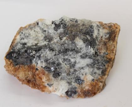 Galenit (bleigrau) mit Quarz (bräunlich) und Baryt (weiß) aus dem Karlstollen bei Badenweiler Handstück eines rautenförmigen Gesteins, in Großaufnahme fotografiert. Das Gestein ist an den Rändern bräunlich, sonst weißlich bis dunkelgrau kristallisiert.