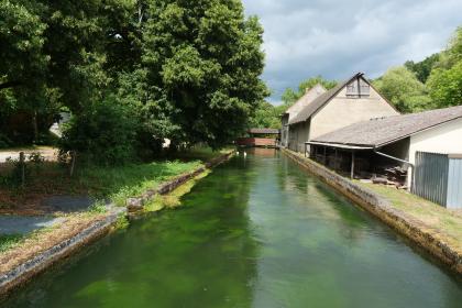 Teilabfluss aus dem Aachtopf im nördlichen Werkkanal Blick auf einen zum Betrachter fließenden, eingefassten Wasserlauf. Rechts der Einfassung stehen Gebäude, am linken Ufer Bäume und Gebüsch.