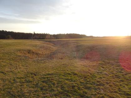 Uvala (Dolinenkette) auf einer Wiese bei Zang, Lkr. Heidenheim, Östliche Schwäbische Alb Zu sehen ist eine große, bis zum Hintergrund reichende Wiese. In der Mitte sind tiefe, grabenartige Verwerfungen erkennbar. Rechts außen zeigen sich durch die tiefstehende Sonne Lichtreflexe.