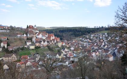 Nagoldtal bei Altensteig am Rand des Nordschwarzwalds Blick auf eine Stadt, die sich auf zwei Anhöhen sowie im Tal dazwischen verteilt. Die Anhöhe links ist höher und steiler, die Häuser stehen teils auf Stützmauern. Im Hintergrund sieht man Wald sowie eine teils offene, teils bewaldete Hochfläche.