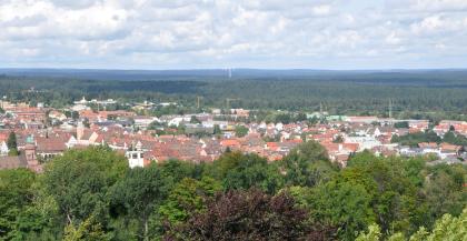 Blick von der Friedrichshöhe bei Freudenstadt nach Norden über die bewaldeten Schwarzwald-Randplatten Aus großer Höhe blickt man über Waldstreifen sowie eine größere Siedlung. Im Hintergrund sind bewaldete Höhen mit Windrädern zu erkennen.