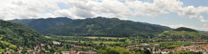 Schwarzwaldrand bei Staufen Panoramabild einer besiedelten, grünen Landschaft mit hohen bewaldeten Bergrücken links vorn sowie im Hintergrund. Rechts erhebt sich ein niedrigerer, nur auf der Kuppe bewaldeter Berg.