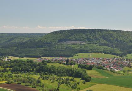 Baaralb-Schichtstufe bei Seitingen-Oberflacht Von erhöhtem Standpunkt aus blickt man auf eine von Waldzungen und einer Ortschaft unterbrochenen Acker- und Grünlandschaft. Dahinter erhebt sich ein steiler, bewaldeter Höhenrücken, gestört von einem Steinbruch.