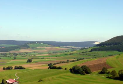 Wartenberg, Donautal und Baaralb bei Geisingen Von erhöhtem Standpunkt aus blickt man über eine sehr wellige, nach rechts und zum Hintergrund hin ansteigende Landschaft mit Acker- und Grünflächen. Dahinter sind ein langer, flacher Höhenzug mit offenem Steinbruch sowie rechts ein Steilhang erkennbar..