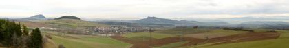 Panoramablick von der Lochhütte bei Tengen nach Ostnordost bis Südsüdost Panoramablick auf ein wannenförmiges Mosaik von Nutzflächen; durchzogen von Stromleitungen und Masten. Im Mittelgrund liegt eine Siedlung, links daneben ein auf der Kuppe bewaldeter Hügel. Im Hintergrund sind mehrere Vulkanberge erkennbar.
