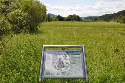 Brudertal östlich von Engen Blick auf eine blühende Wiese, die zum Hintergrund hin ansteigt. Dahinter Wald, bewaldete Hänge und Berge sowie eine Autobahnbrücke. Im Vordergrund ist eine Schautafel angebracht.,