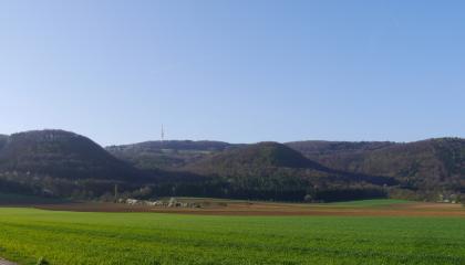 Blick vom Klettgauer Tal östlich von Klettgau-Geißlingen zum Kleinen Randen Hinter einer fast ebenen Acker- und Grünlandschaft staffeln sich verschiedene, teils kegelförmige Erhebungen. Links der Bildmitte steht auf einer dieser Anhöhen ein Sendemast.