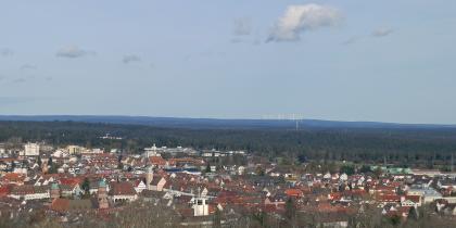 Blick von der Friedrichshöhe bei Freudenstadt nach Norden über das Stadtgebiet und die bewaldeten Schwarzwald-Randplatten nach Norden, zum Windpark Nordschwarzwald Das Bild zeigt im Vordergrund eine große Stadt und anschließende, weite Nadelwälder. Im Hintergrund ist eine Hochebene mit Windrädern erkennbar.