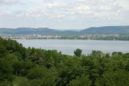 Aussicht von den Moränenhügeln bei Gaienhofen-Gundholzen über den Zeller See auf die Höhenzüge des Bodanrücks (rechts) und der Homburg im Hintergrund Blick über einen Wald auf einen See. Im Hintergrund sind Siedlungen sowie bewaldete Höhenzüge erkennbar.