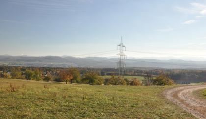 Blick von den höchsten Lagen des Dinkelbergs beim Hohen Flum (536 m ü. NHN) nach Süden über das Hochrheintal hinweg zum Schweizer Jura Blick auf hochgelegene Wiesen mit Baumbestand im Mittelgrund. Am Horizont verlaufen bewaldete Bergrücken.