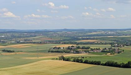 Blick von der Heuchelberger Warte über das Neckarbecken auf den der Keuperschichtstufe vorgelagerten Wunnenstein Weiter Blick aus großer Höhe auf eine wellige Landschaft mit zahlreichen Ackerflächen, Waldstreifen und kleineren Siedlungen. Im Hintergrund, in der Bildmitte, ist ein vorgelagerter Kegelberg erkennbar. Dahinter liegen bewaldete Höhen.