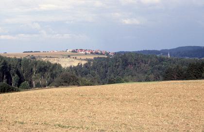 Blick von der Lettenkeuperfläche über das Stunzach- und Eyachtal mit Muschelkalksteinbruch und bewaldeten Talhängen nach Nordosten auf die Gäuflächen bei Haigerloch-Stetten Bewaldete Talhänge begrenzen einen im Vordergrund ausgebreiteten, gelblich braunen Acker. Links taucht ein Steinbruch über den Waldspitzen auf sowie eine leicht gewölbte, besiedelte Ebene. Rechts steigt eine größere Anhöhe auf.