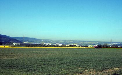 Lettenkeupergäu bei Empfingen; links die Keuper-Schichtstufe An eine waagrecht verlaufende, grüne Ackerfläche schließen sich gelbe Rapsfelder und links zwei bewaldete Höhenzüge an. Eine ferne Ebene und ein türkisblauer Himmel vervollständigen das Bild.