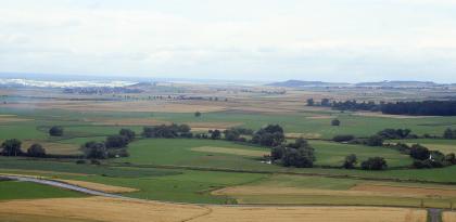 Flussschlingen der Donau bei Geisingen-Gutmadingen Der Blick geht über eine weite Ebene. Sie ist teils grün, teils gelb-braun gefärbt. In der Bildmitte windet sich ein Fluss, gesäumt von Bäumen, von rechts nach links. Er bildet dabei s-förmige Schlingen.