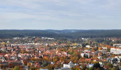 Blick vom Aussichtsturm auf der Wanne bei Villingen nach Westnordwesten zum Buntsandstein-Schwarzwald Von erhöhtem Standort blickt man über Hausdächer, Tor- und Kirchtürme einer größeren Stadt auf ein im Hintergrund verlaufendes Band mit bewaldeten Bergen.