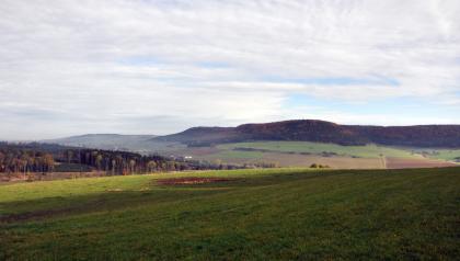 Im Nordosten sieht man jenseits des Kötachtals die bewaldete Oberjura-Schichtstufe der Baaralb Blick über teilweise schattige, hochgelegene Wiesen auf im Hintergrund ansteigende, an den Kuppen bewaldete Berghänge. Links schiebt sich eine Waldspitze zwischen Wiese und Hanglagen.