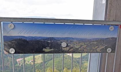 Panoramatafel auf dem Buchkopfturm bei Oppenau-Maisach Blick auf ein in großer Höhe befindliches Metallgeländer eines Aussichtsturmes. Am Geländer ist ein Panormabild mit den umgebenden Bergen und Ortschaften angebracht.