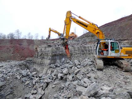 Gipsabbau in den Grundgipsschichten des Gipsbruchs Crailsheim-Triensbach Gezeigt werden mehrere Bagger, die in einem Steinbruch Gestein abbauen. Im Vordergrund wird eine niedrige Wand weiter zerkleinert, loses Gestein und Schutt liegt verstreut davor.