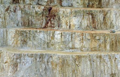 Abbauwand im Steinbruch Blaustein-Wippingen Blick auf eine abgestufte Steinbruchwand mit drei waagrecht verlaufenden Fahrstraßen und teilweise angehäuften Schutthalden. Das Gestein ist mehrfarbig, von hellgrau bis braun.